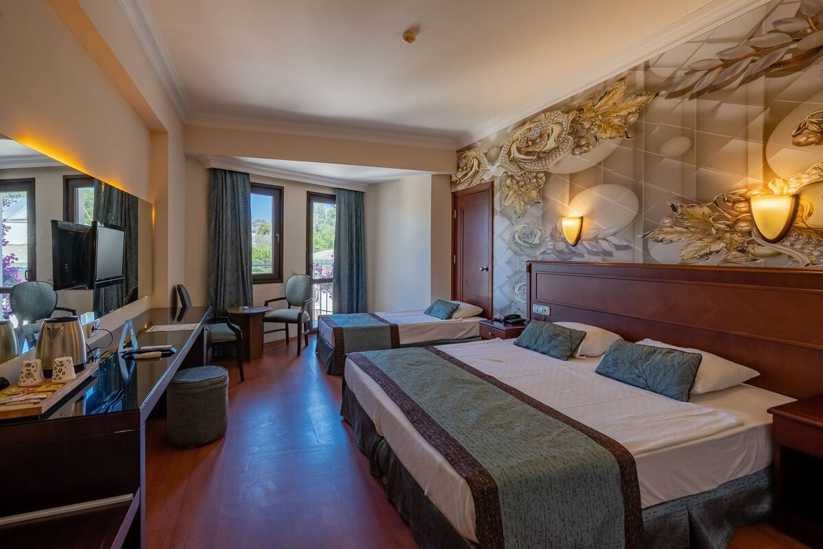 A hotel room with two beds, a desk, a chair, a television, and a view of the outdoors.