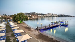 Un hotel frente a la playa con filas de tumbonas y un muelle que se adentra en el agua.