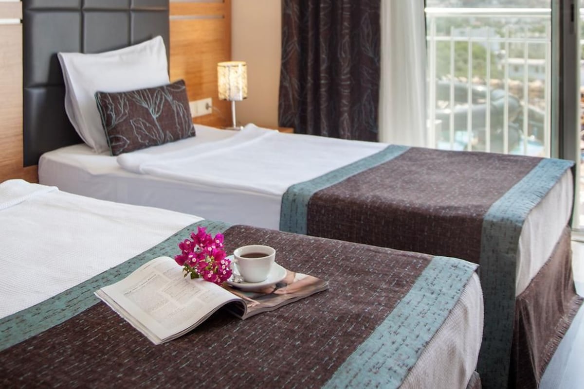 Quarto de hotel com duas camas, uma janela com cortinas, uma mesa de cabeceira com abajur e vista para a cidade.