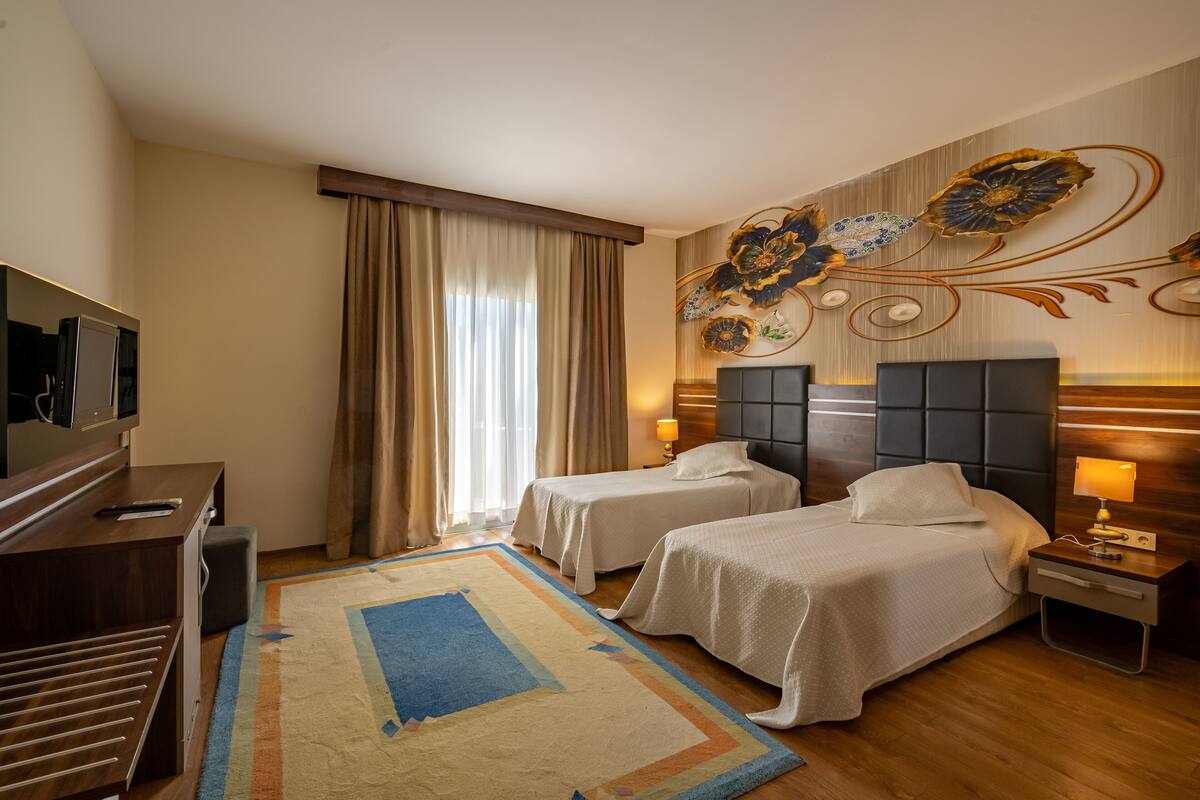 A hotel room with two beds, a desk, a TV, and a decorative wall.