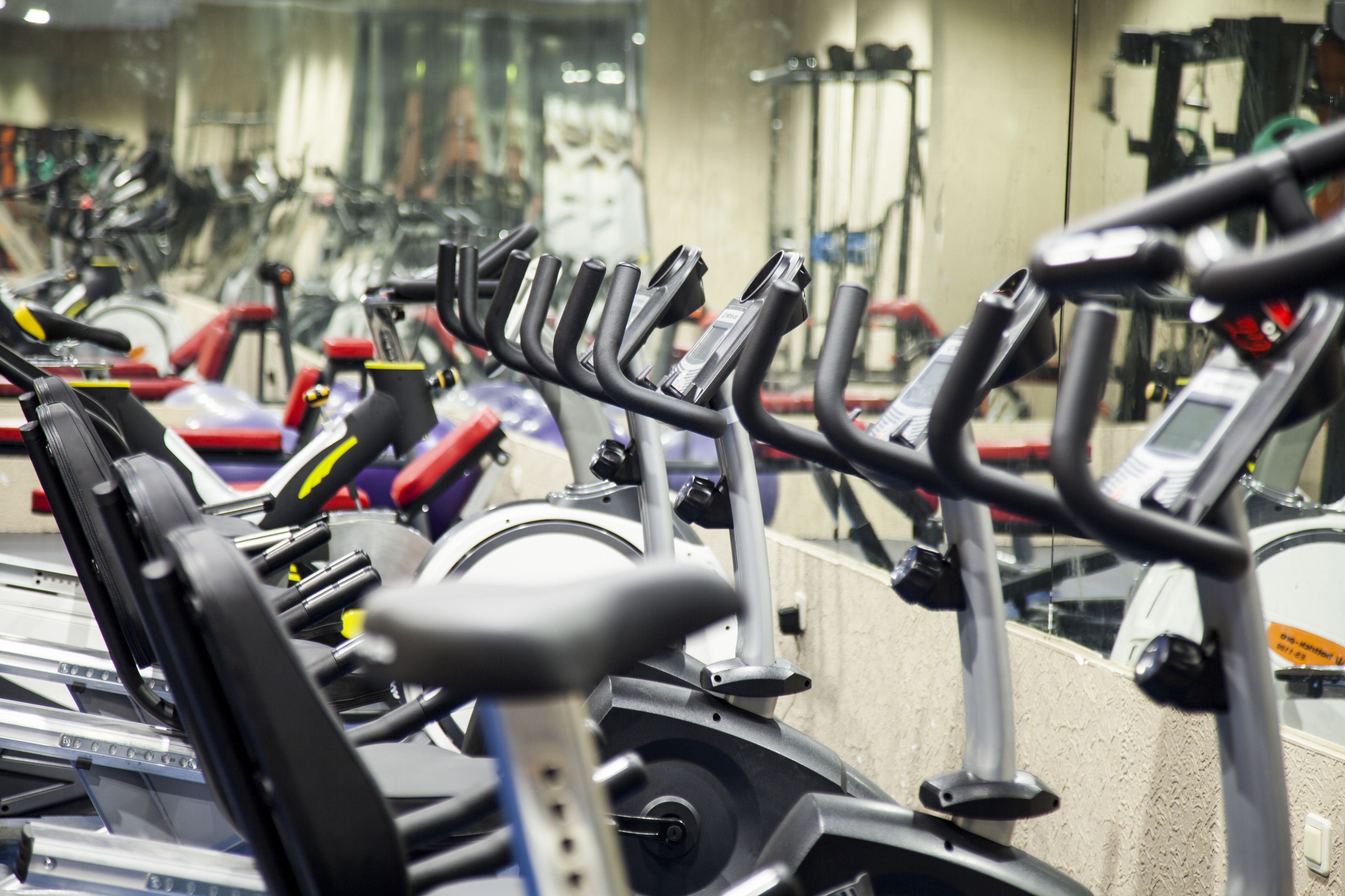 En række stillestående cykler i et fitnesscenter med spejle på væggene.