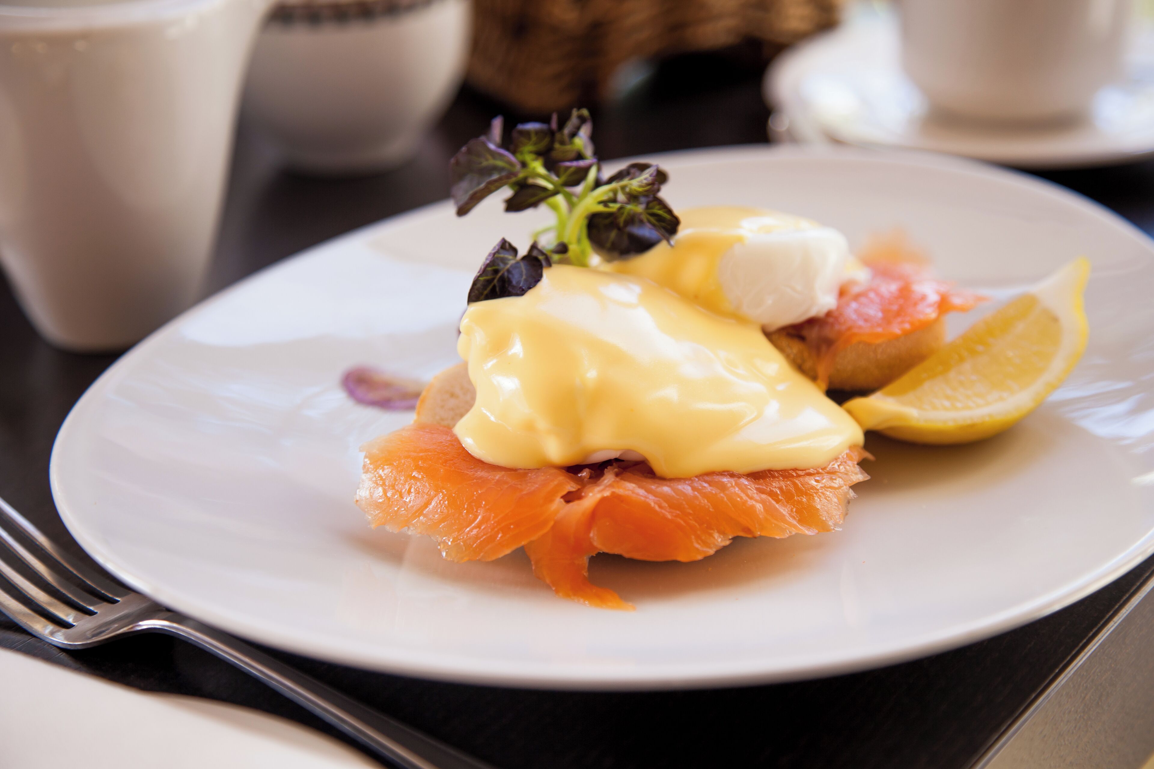 A plate with smoked salmon, hollandaise sauce, and a lemon slice.