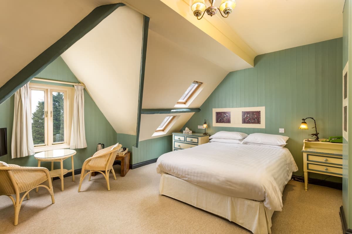 Ein Schlafzimmer mit schrägen Wänden, einem Bett, einem kleinen Tisch, zwei Stühlen, einem Nachttisch und einer Lampe.