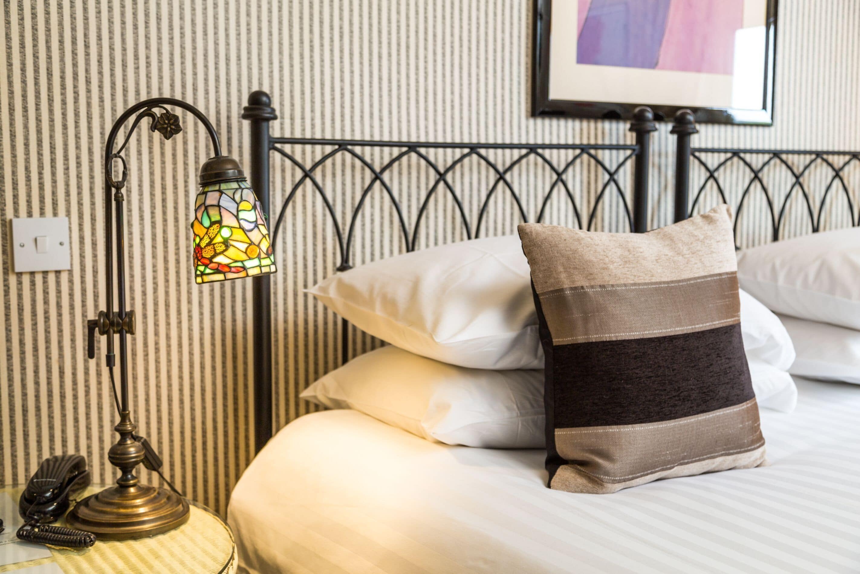 Una cama bien hecha con almohadas blancas y a rayas, una pared a rayas y una lámpara de estilo vintage sobre una mesita de noche.