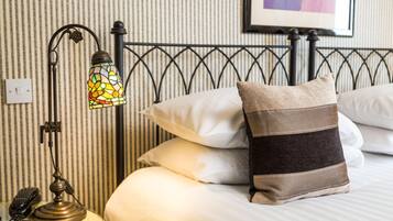Una cama bien hecha con almohadas blancas y a rayas, una pared a rayas y una lámpara de estilo vintage sobre una mesita de noche.
