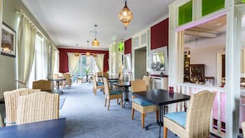 Un comedor con sillas y mesas de mimbre, lámparas colgantes y vistas al jardín a través de amplios ventanales.