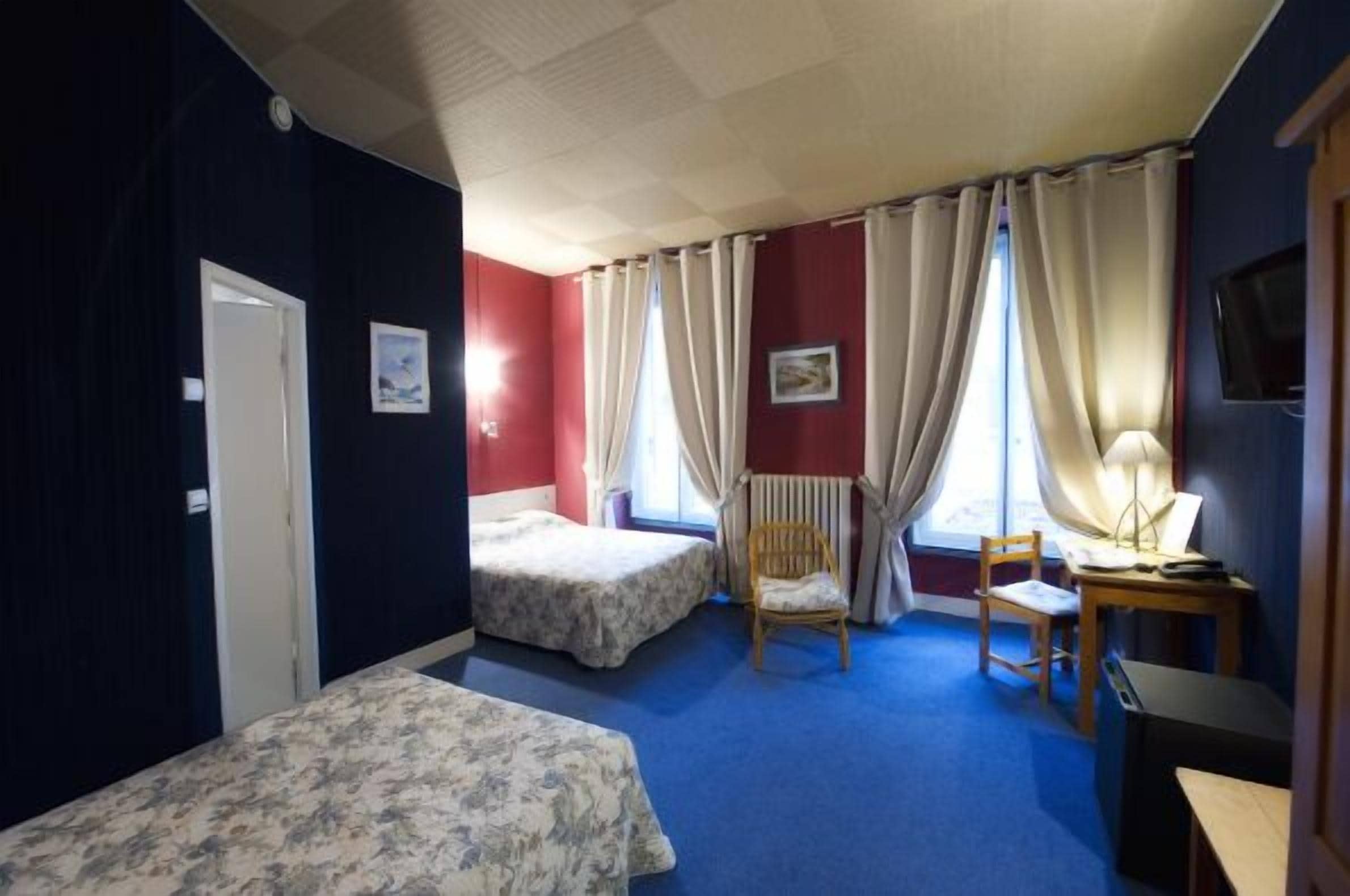 A hotel room with two single beds, a desk with a lamp, a chair, and a television on the wall.