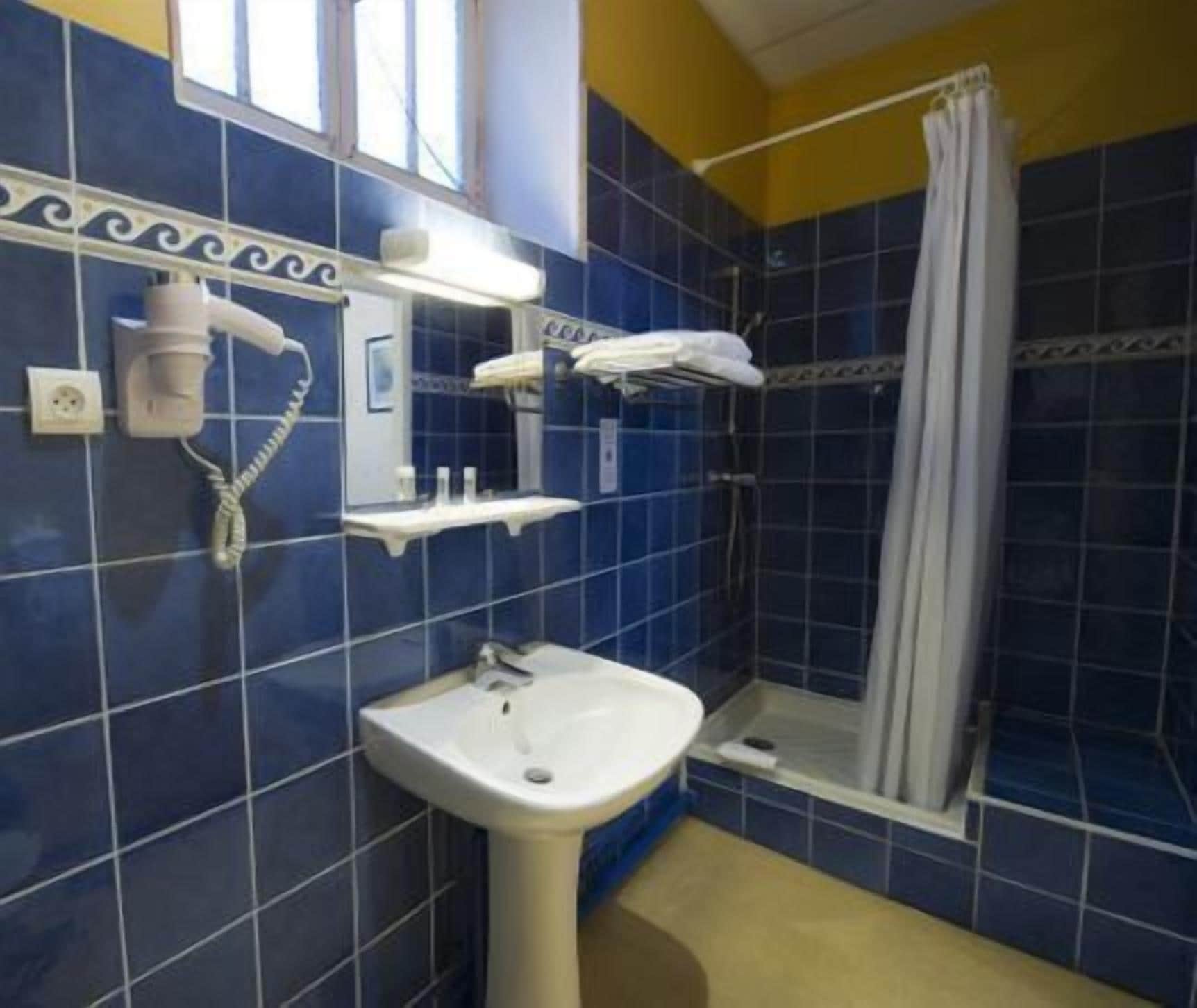 Un baño con lavamanos blanco, ducha con cortina y un perchero para toallas.