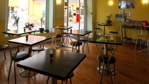 A cafe with multiple tables and chairs, potted plants, and a view of the street outside.