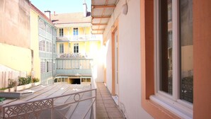 A narrow alleyway with a metal railing, a building with a balcony, and a window on the right.