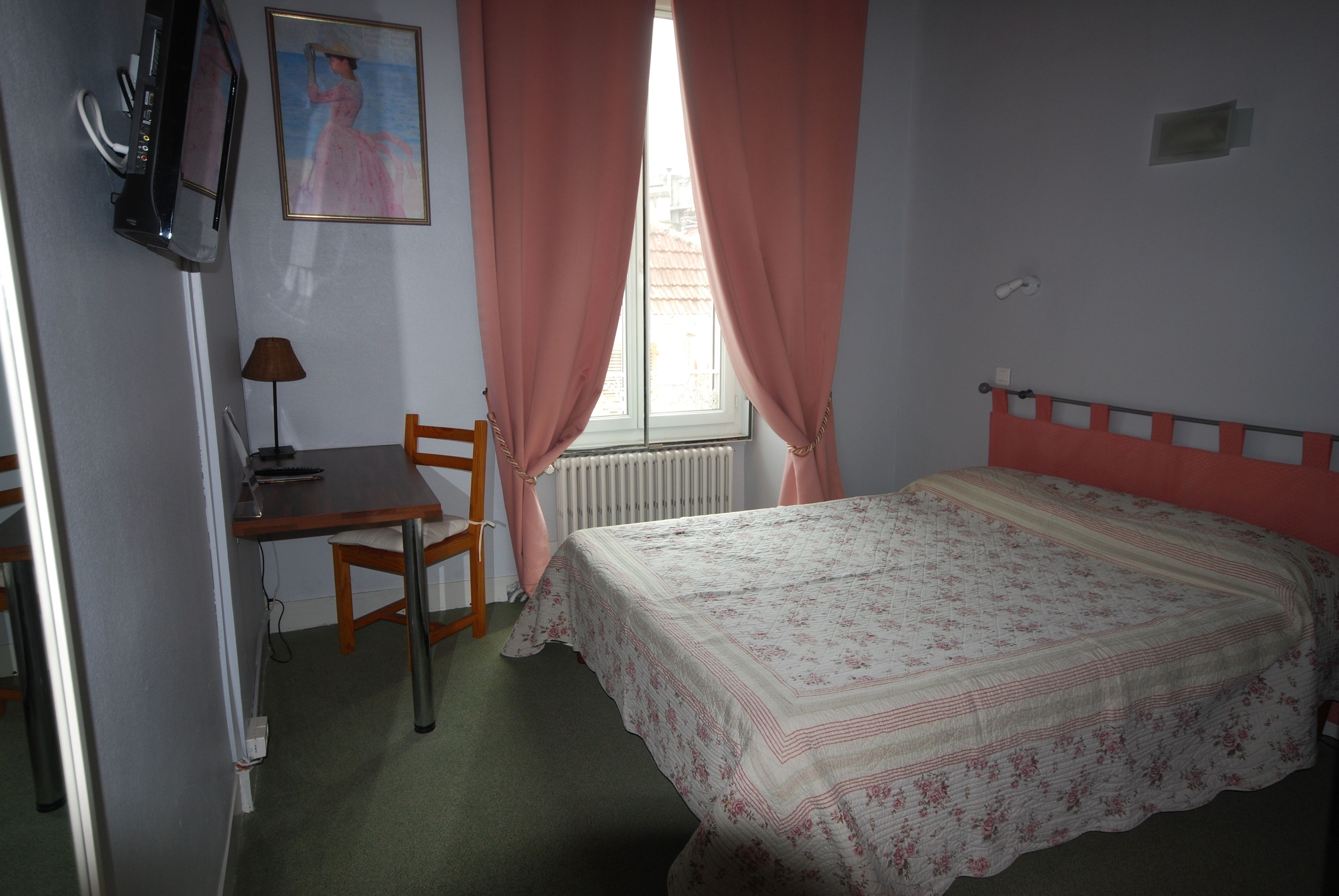 A bedroom with a bed, a desk, a chair, a radiator, and a window with curtains.