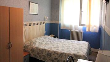 A bedroom with a bed, a wardrobe, a desk, a radiator, and a window with curtains.