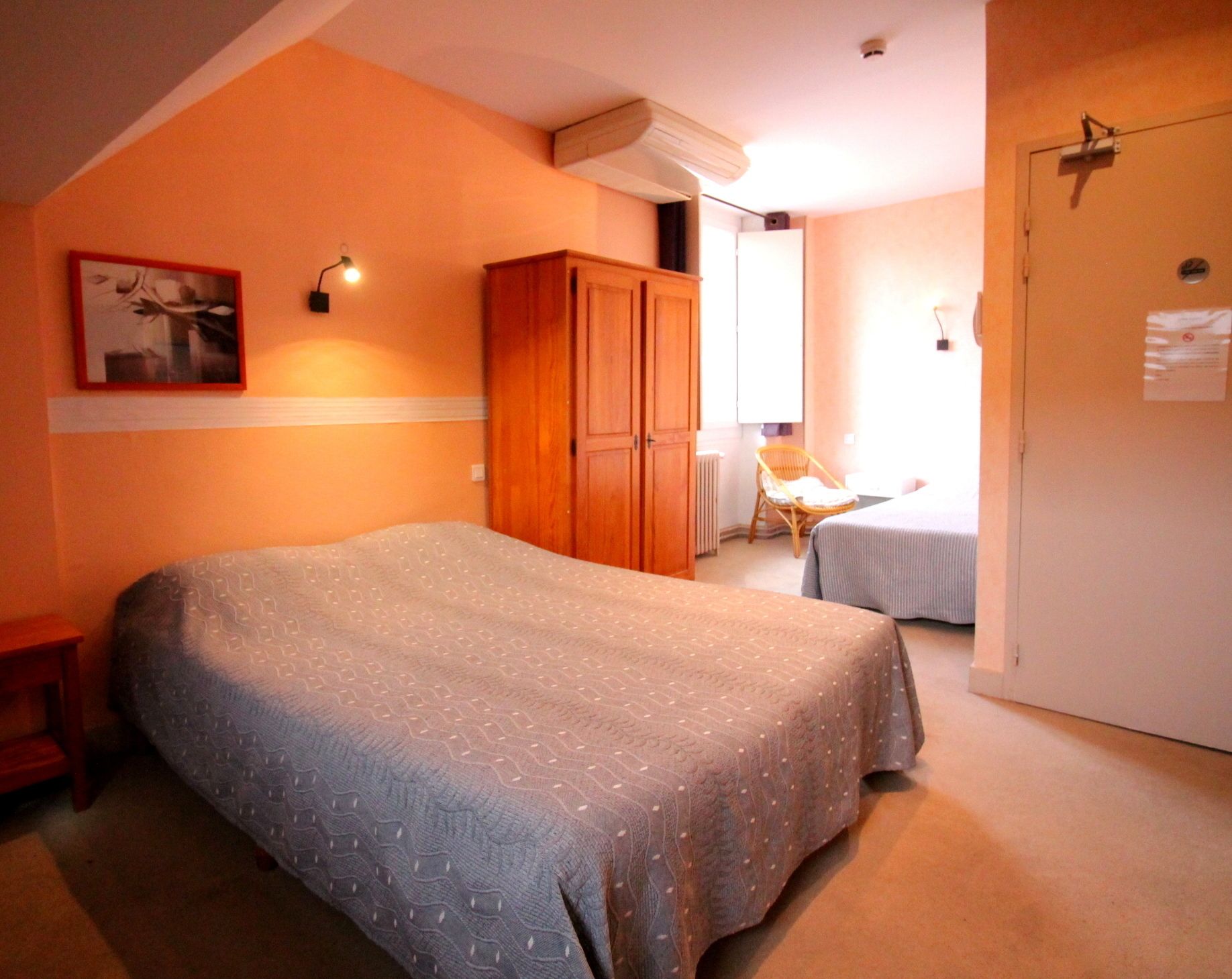 A bedroom with a large bed, a wardrobe, a small table with a chair, and a door with a lock.