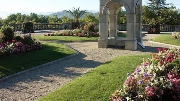 A stone gazebo with arches, surrounded by well-maintained gardens and a clear sky.