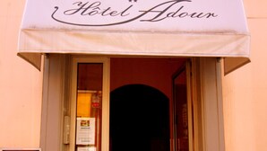 The entrance to Hotel Adour with a white awning and a glass door.