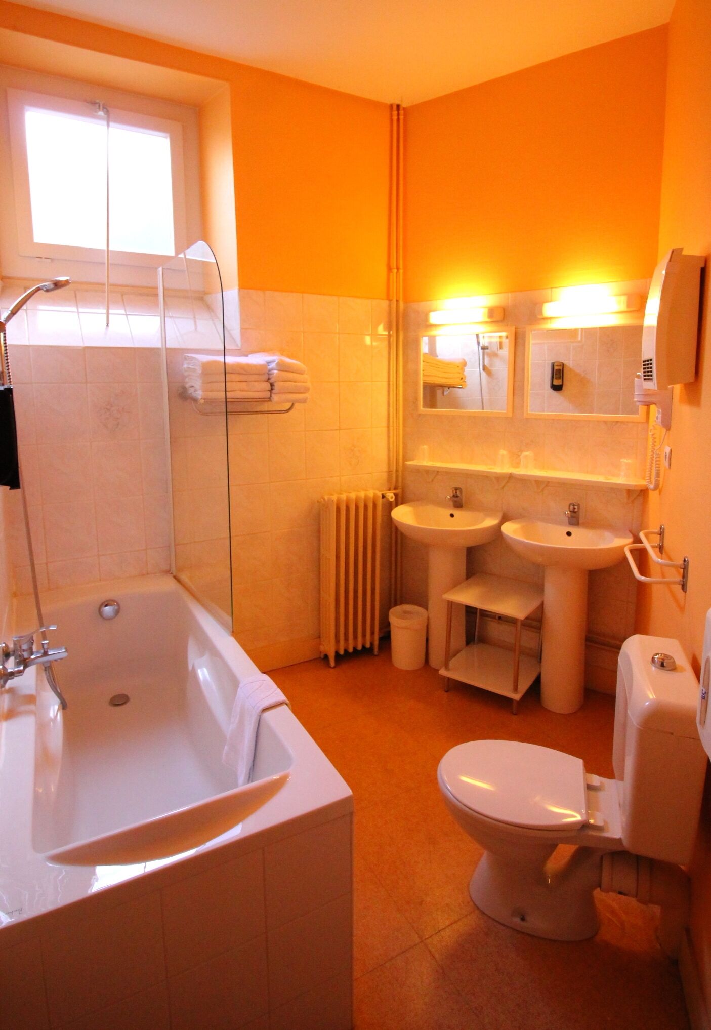 A bathroom with a bathtub, two sinks, a toilet, and a window.
