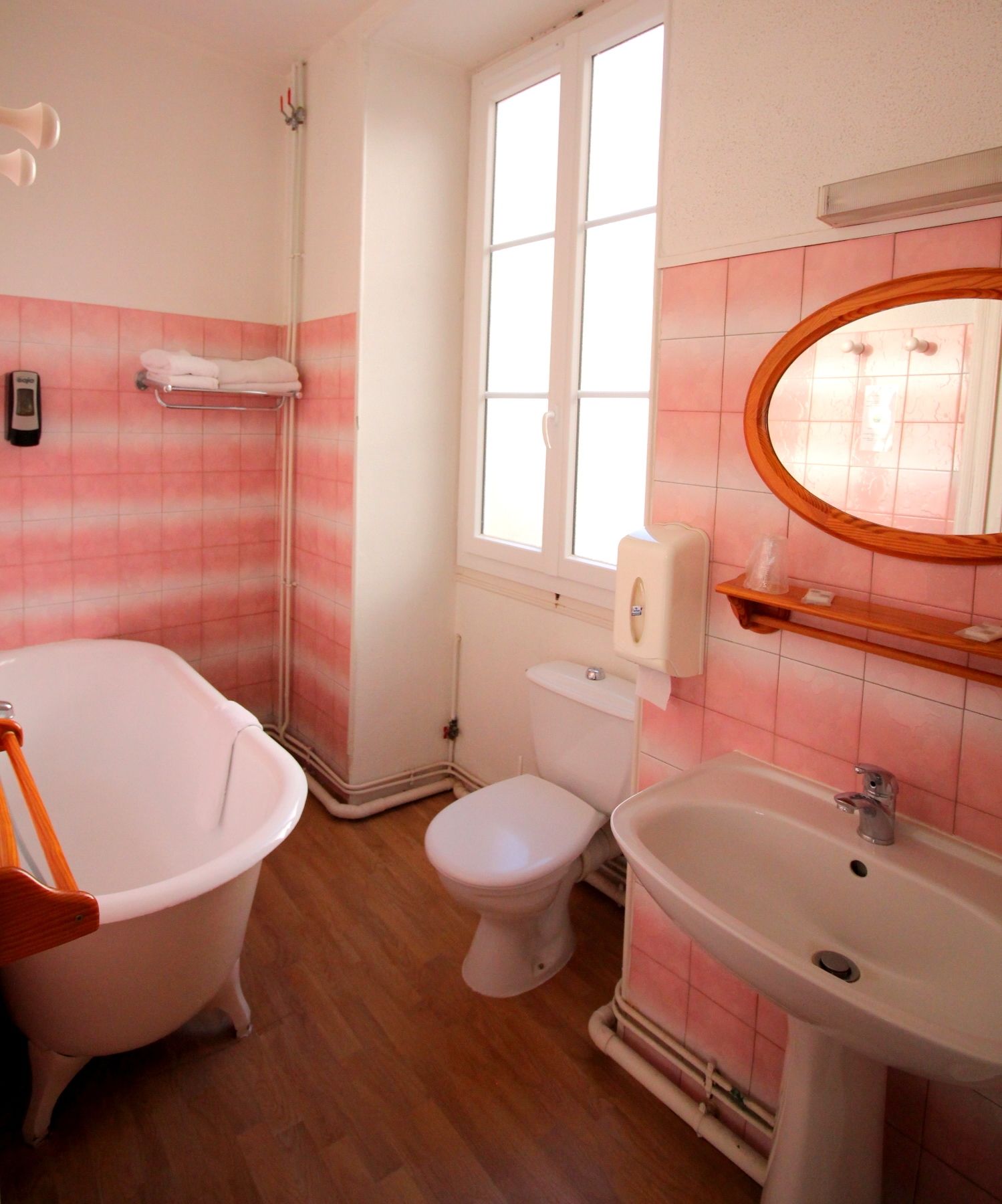 Ein Badezimmer mit einer weißen Badewanne, einer weißen Toilette und einem weißen Waschbecken. Ein Fenster sorgt für natürliches Licht, und über dem Waschbecken befindet sich ein Spiegel.
