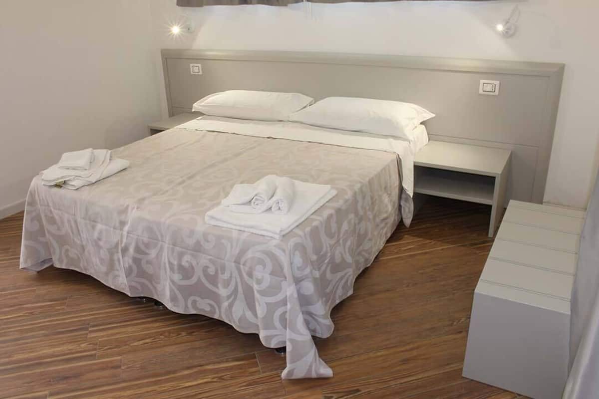 A neatly made bed with a patterned bedspread, a bedside table with a lamp, and a wooden floor.
