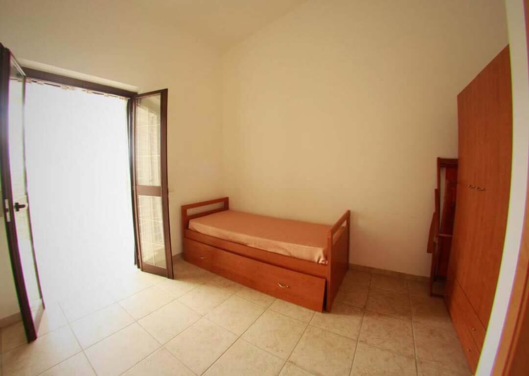 A bedroom with a single bed, a wardrobe, and a door leading to another room.