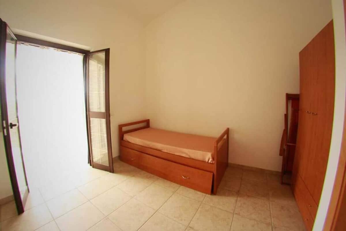 A bedroom with a single bed, a wardrobe, and a door leading to another room.