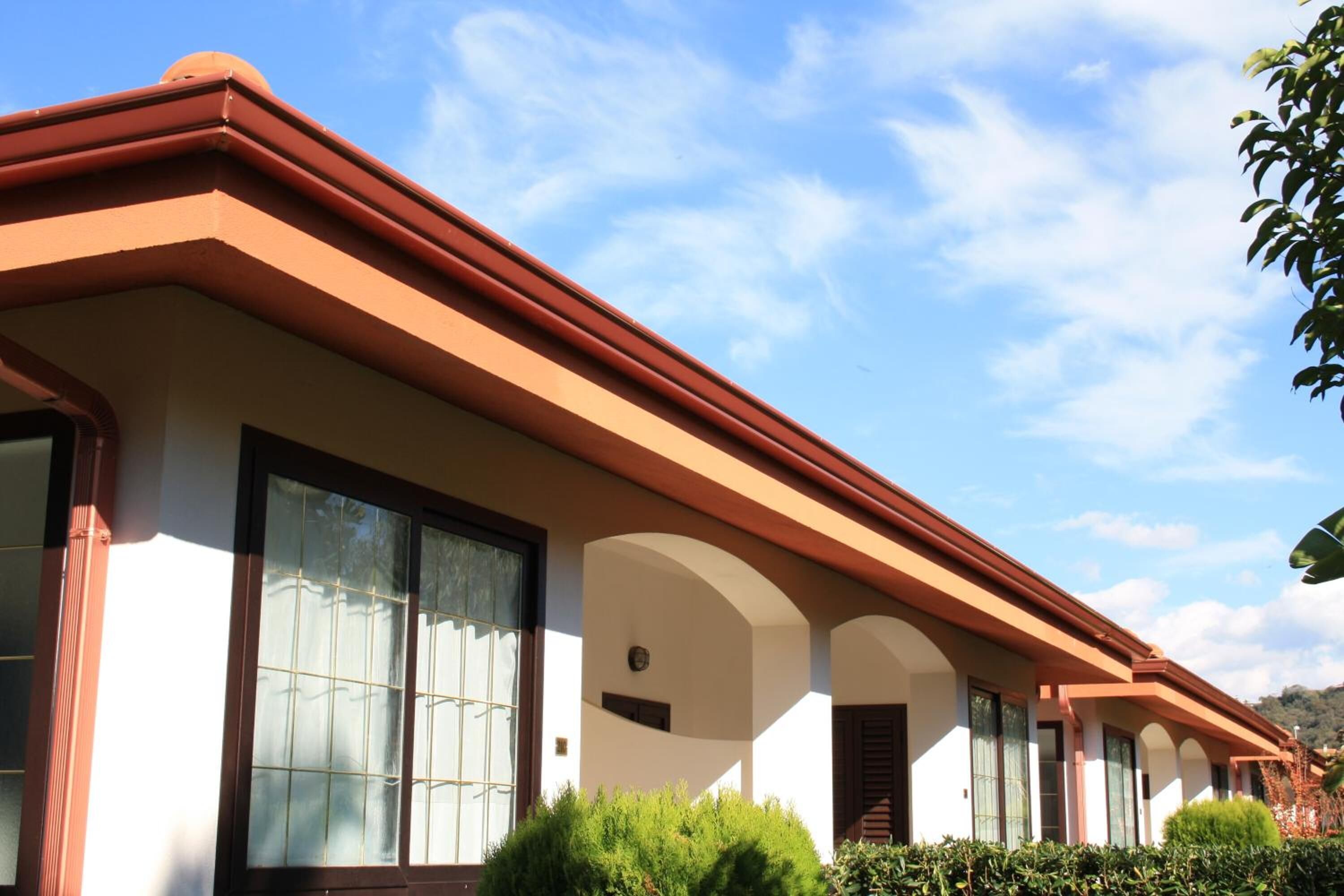 A row of hotel rooms with large windows, a red roof, and a clear blue sky.