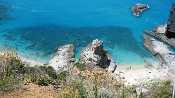 Un paisaje costero con aguas azul cristalino, formaciones rocosas y una playa arenosa.