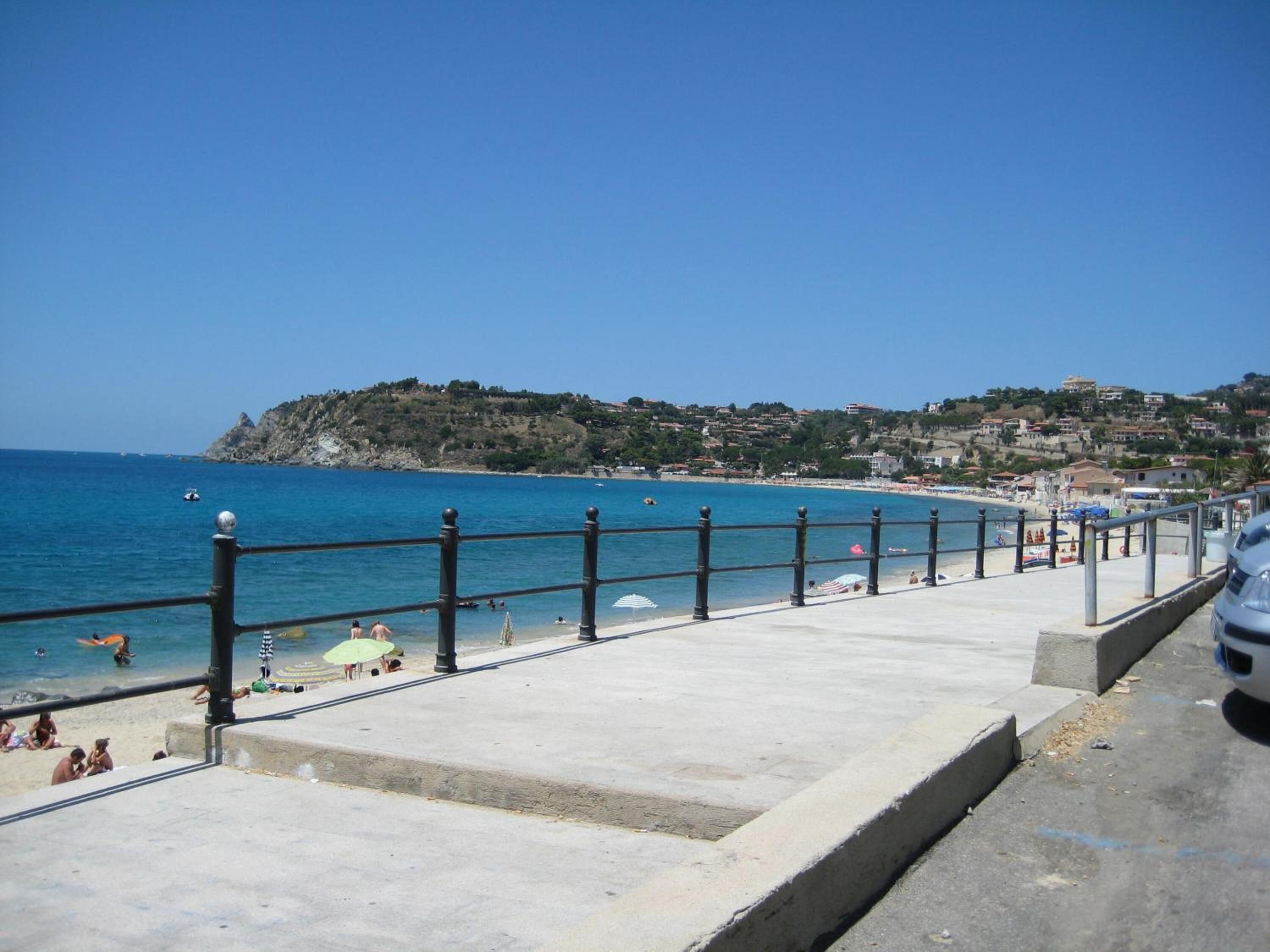 A coastal promenade with a clear view of the sea, a stone pathway, and a row of beach umbrellas.