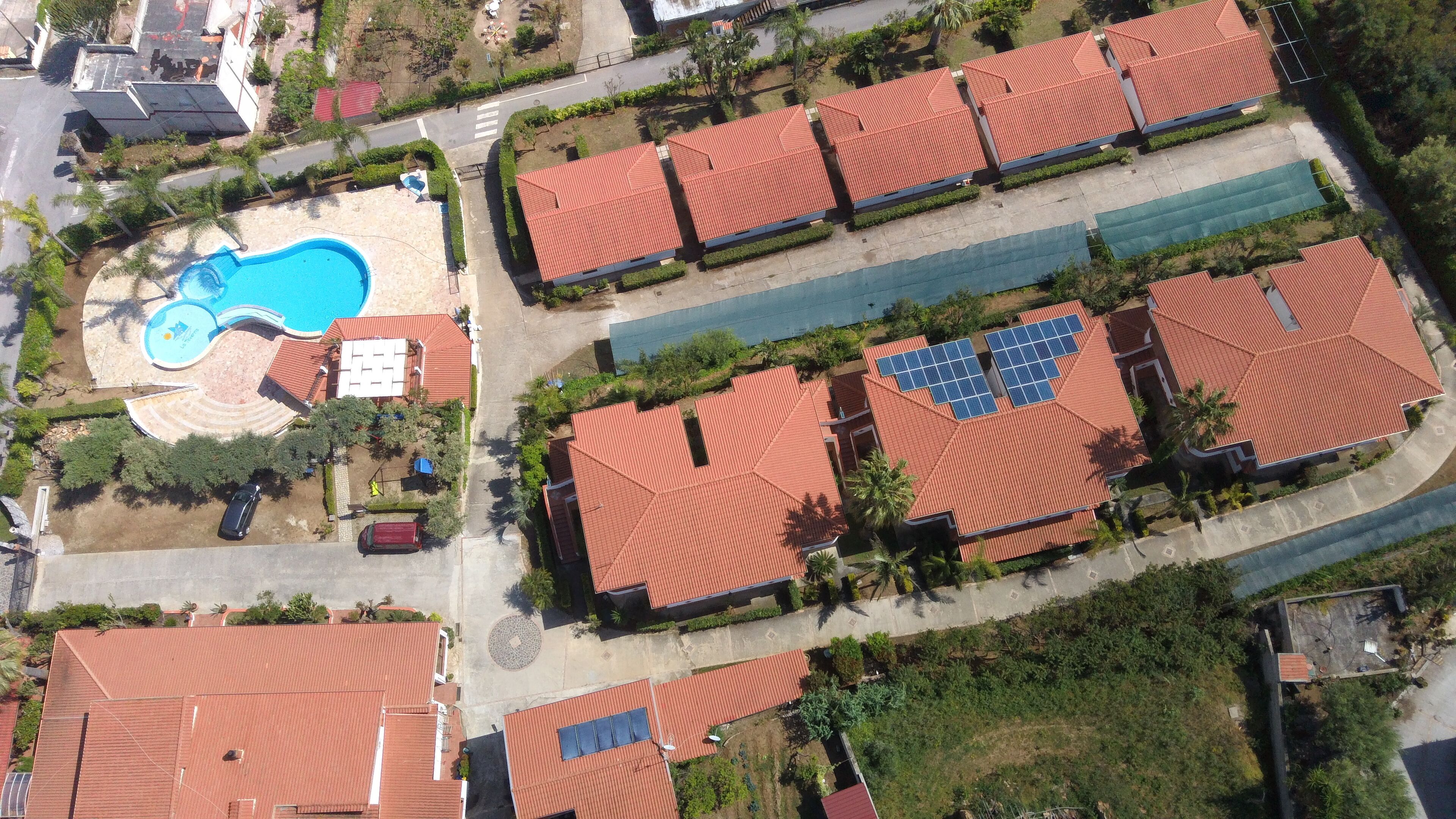 An aerial view of a residential area with multiple houses, a swimming pool, and solar panels on the roofs.