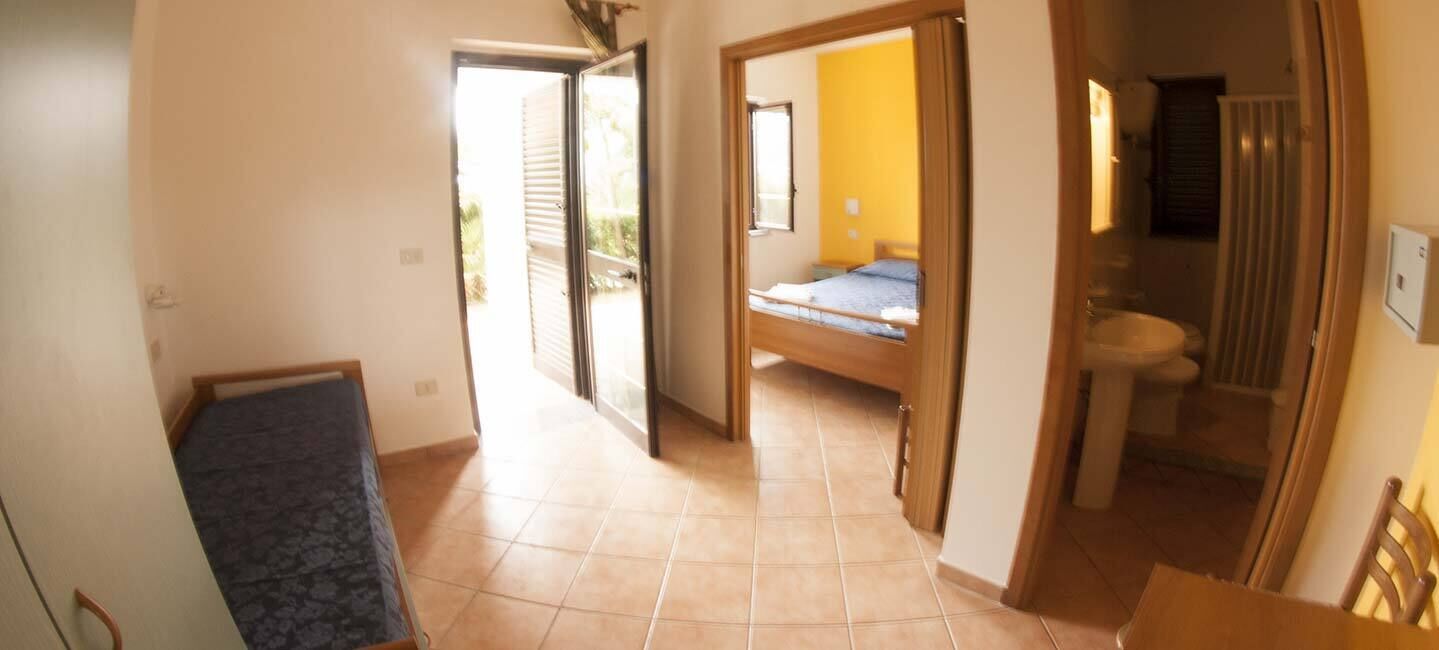 A corridor leading to a bedroom with a bed, a bathroom with a sink and toilet, and a view of the outside.