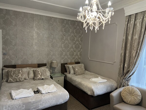 A hotel room with a large bed, two smaller beds, a chandelier, and a view of the outdoors.