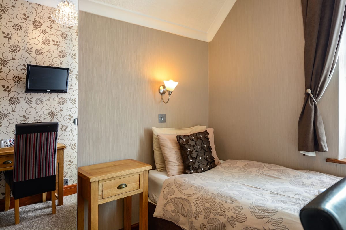 Habitación de hotel con cama, escritorio, silla, televisor montado en la pared y lámpara de pared.