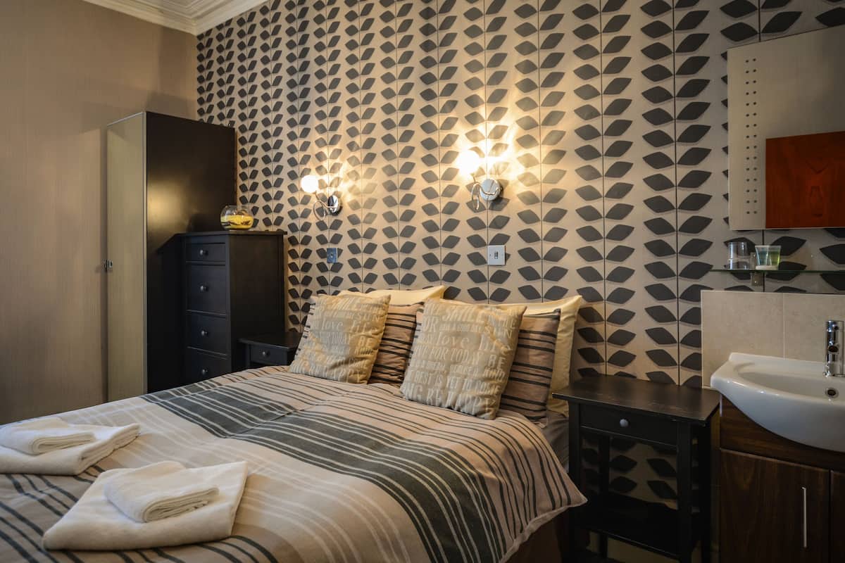 Habitación de hotel con cama, cómoda, mesita de noche y baño con lavabo y espejo.
