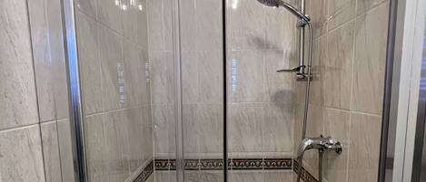 A glass-enclosed shower stall with a handheld showerhead and a wall-mounted faucet.