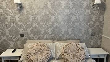 A bedroom with a patterned wallpaper, two bedside lamps, a bed with a decorative headboard, and a nightstand with a remote control.