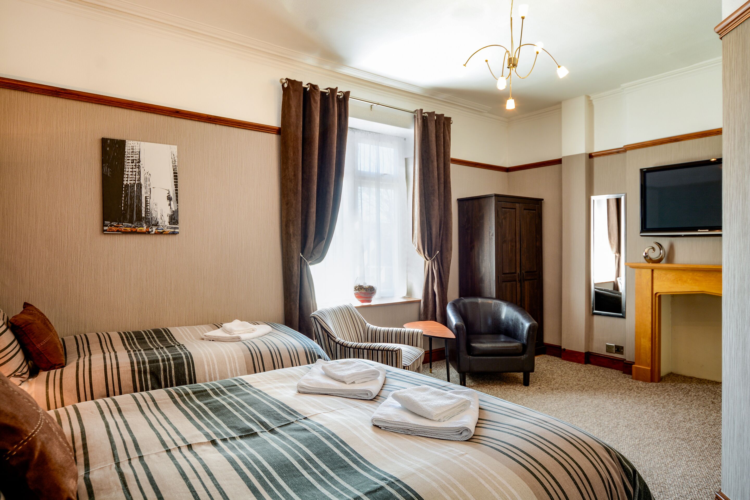 Habitación de hotel con dos camas, televisión, chimenea y ventana con cortinas.