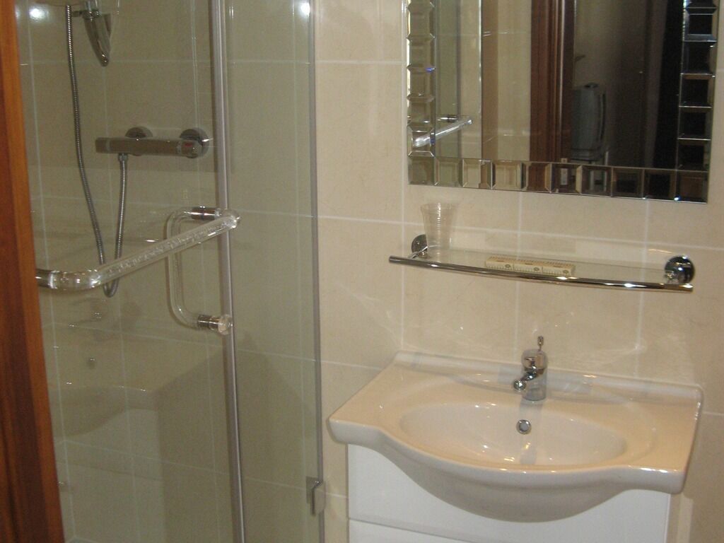 A bathroom with a glass shower enclosure, a sink with a mirror above it, and a shelf above the sink.