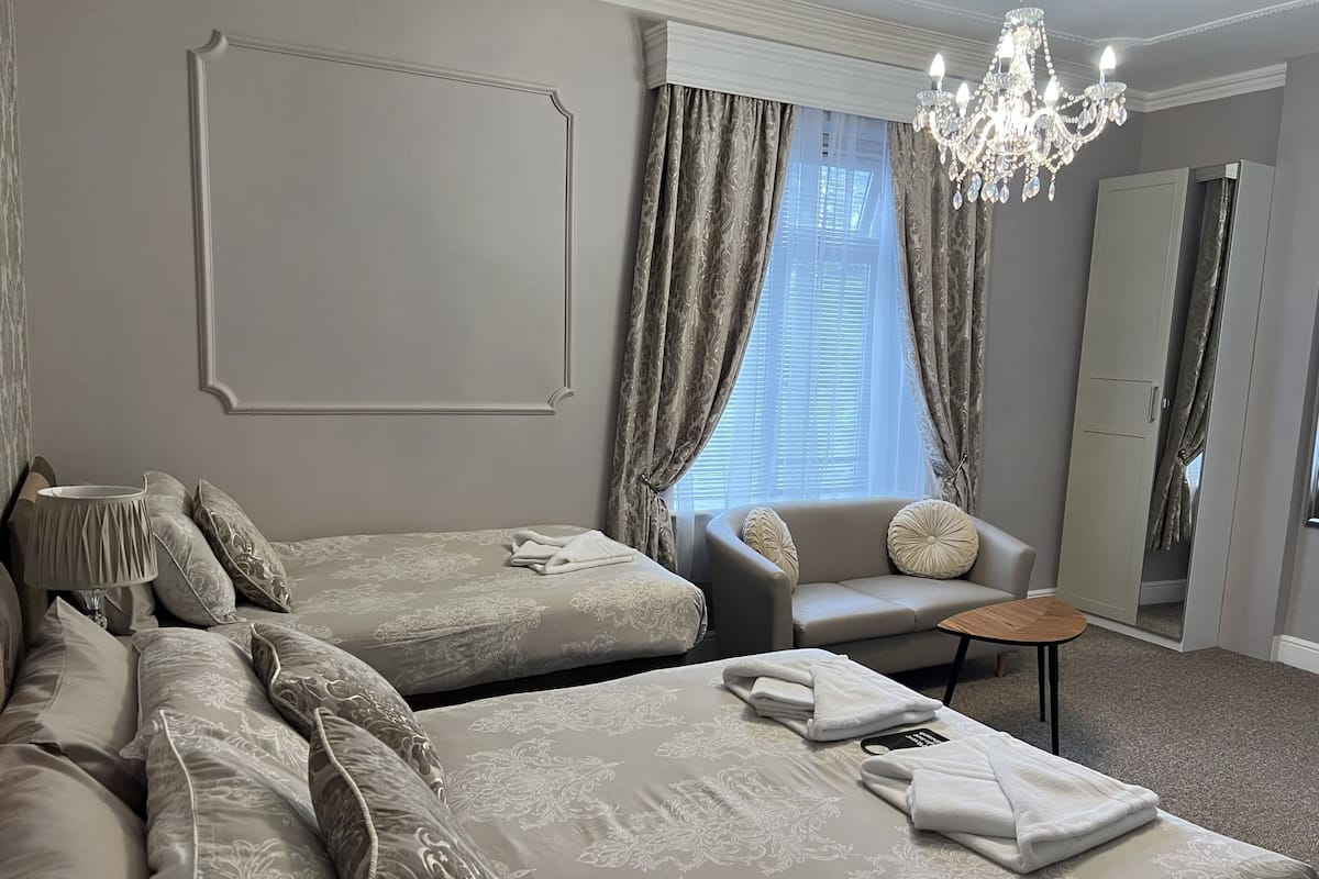 Habitación de hotel con dos camas, un sofá, una mesita, un candelabro y un armario.