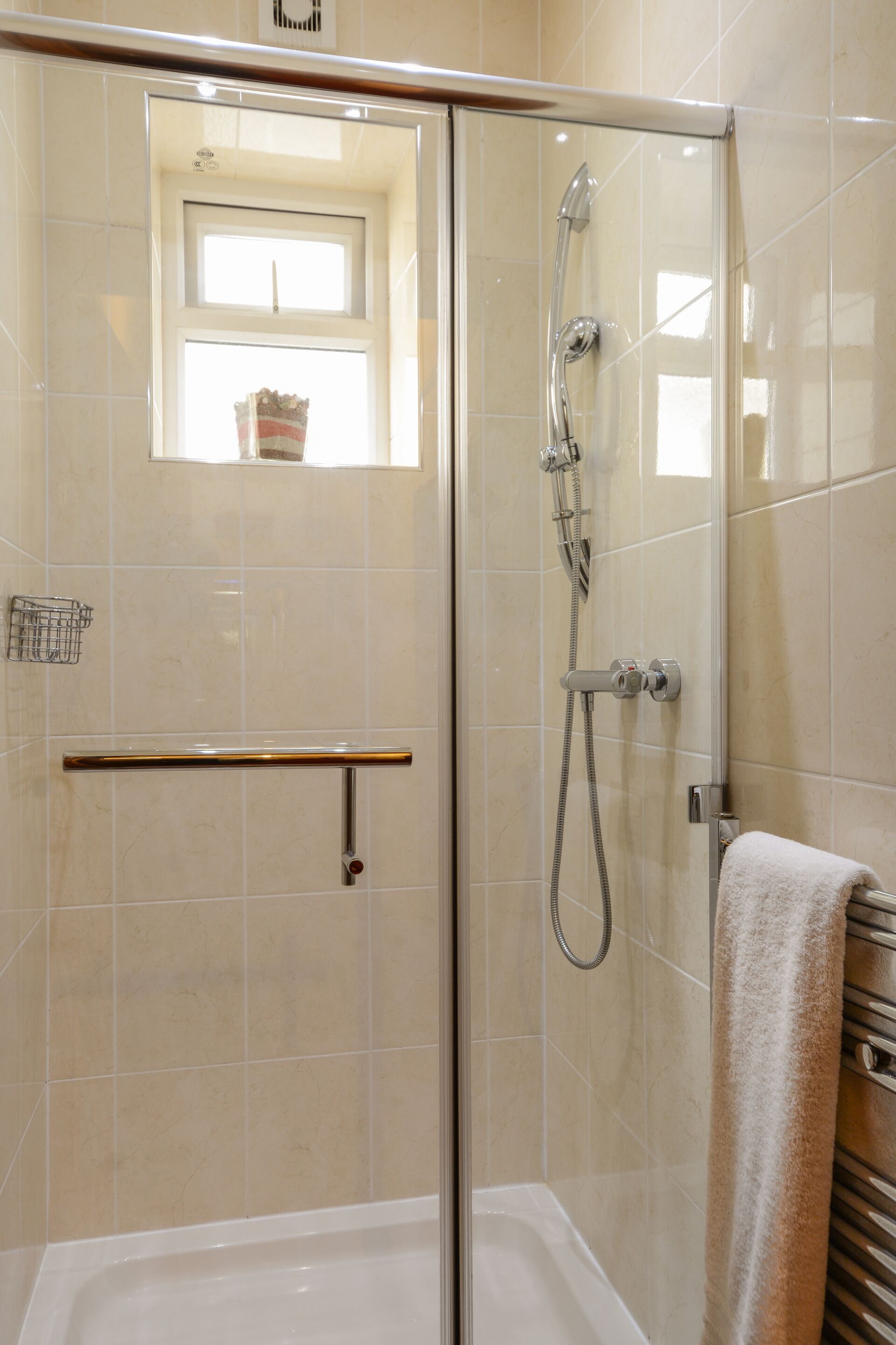 A glass-enclosed shower with a handheld showerhead, a handheld showerhead, and a towel rack with a towel.