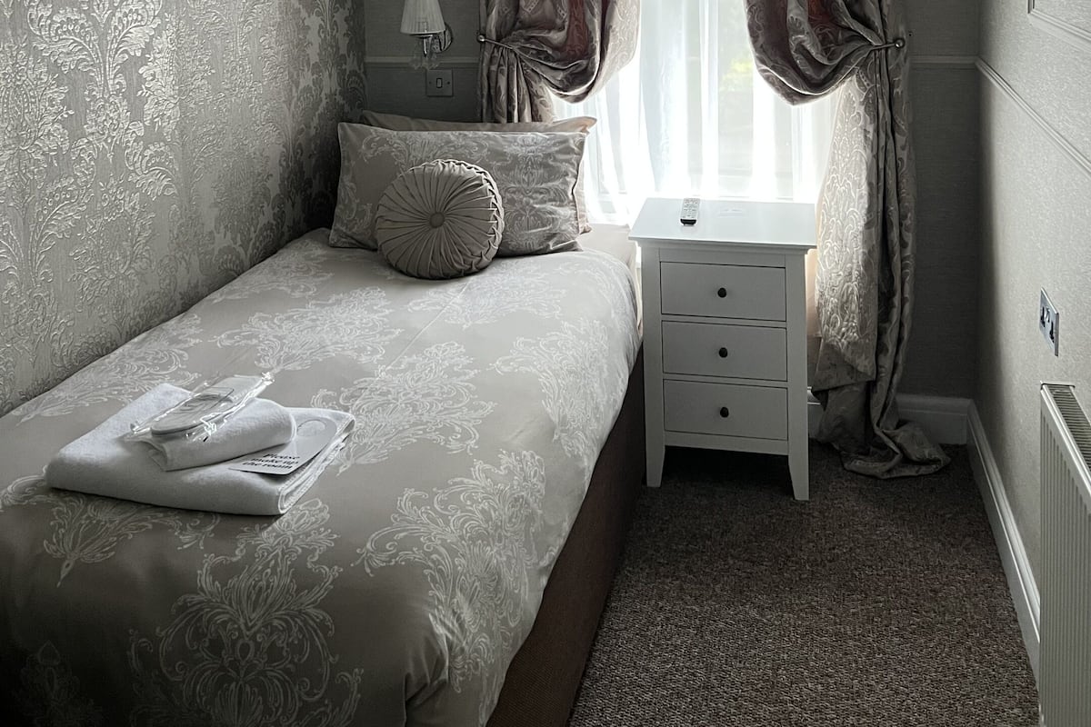 Un dormitorio con cama, mesita de noche, lámpara y cortinas.
