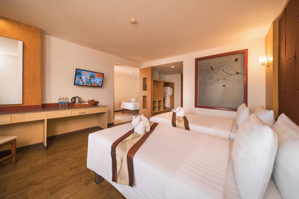 A hotel room with two beds, a desk, a television, and a painting on the wall.
