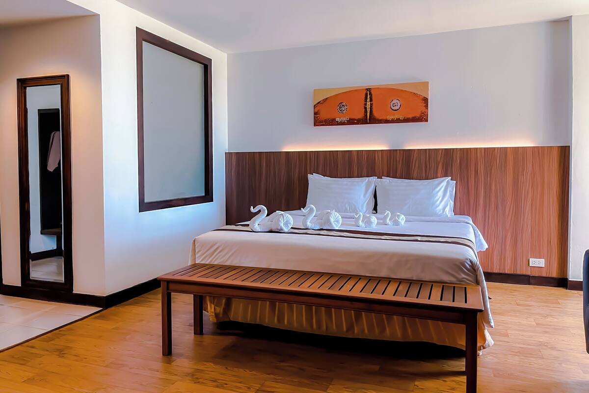 A neatly arranged hotel room with a wooden bed, a bench, and a large mirror.