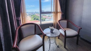 Una habitación con dos sillas de madera, una pequeña mesa redonda con un florero y un amplio ventanal con vista a la ciudad.