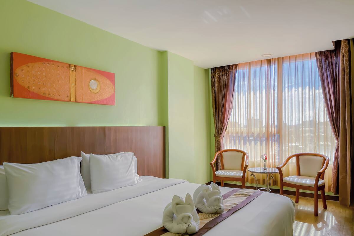 A hotel room with a large bed, two chairs, a small table, and a painting on the wall.