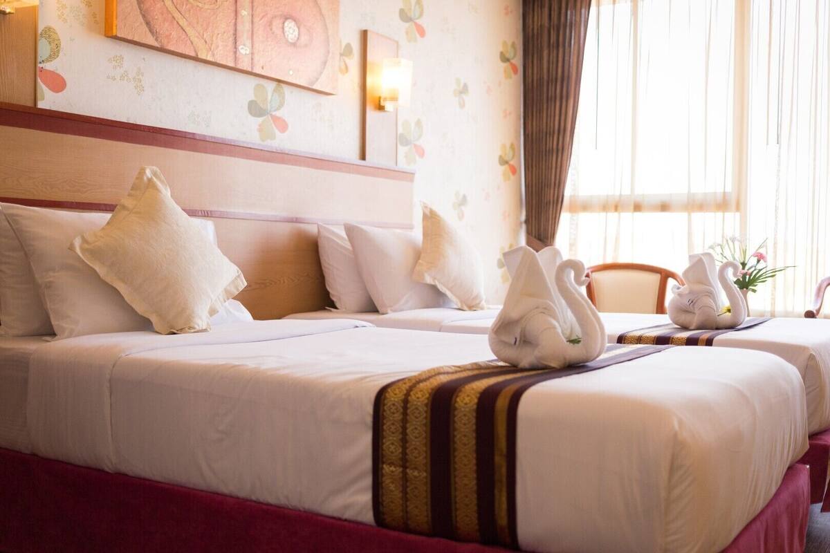 A hotel room with two beds, a wooden headboard, a floral wall design, and a window with curtains.