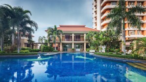 Un hotel con piscina, palmeras y un edificio de varios pisos con balcones.