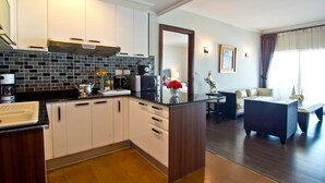 Een moderne keuken met witte kastjes, een zwarte spatwand en een centraal eiland. Er is een zithoek met een bank en salontafel.