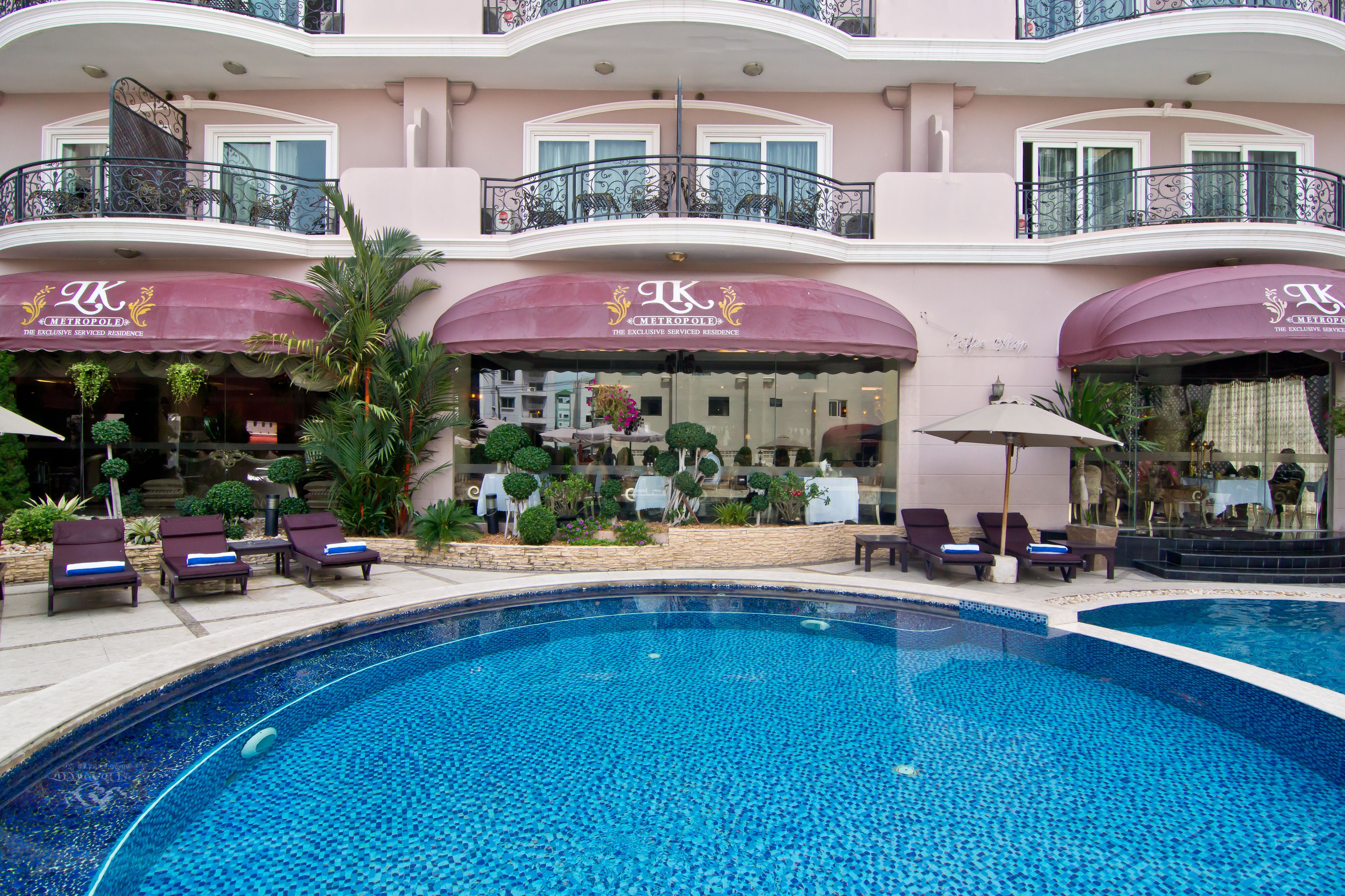 A hotel with a swimming pool, lounge chairs, and a well-maintained garden.