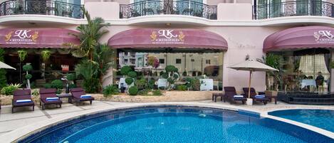 A hotel with a swimming pool, lounge chairs, and a well-maintained garden.