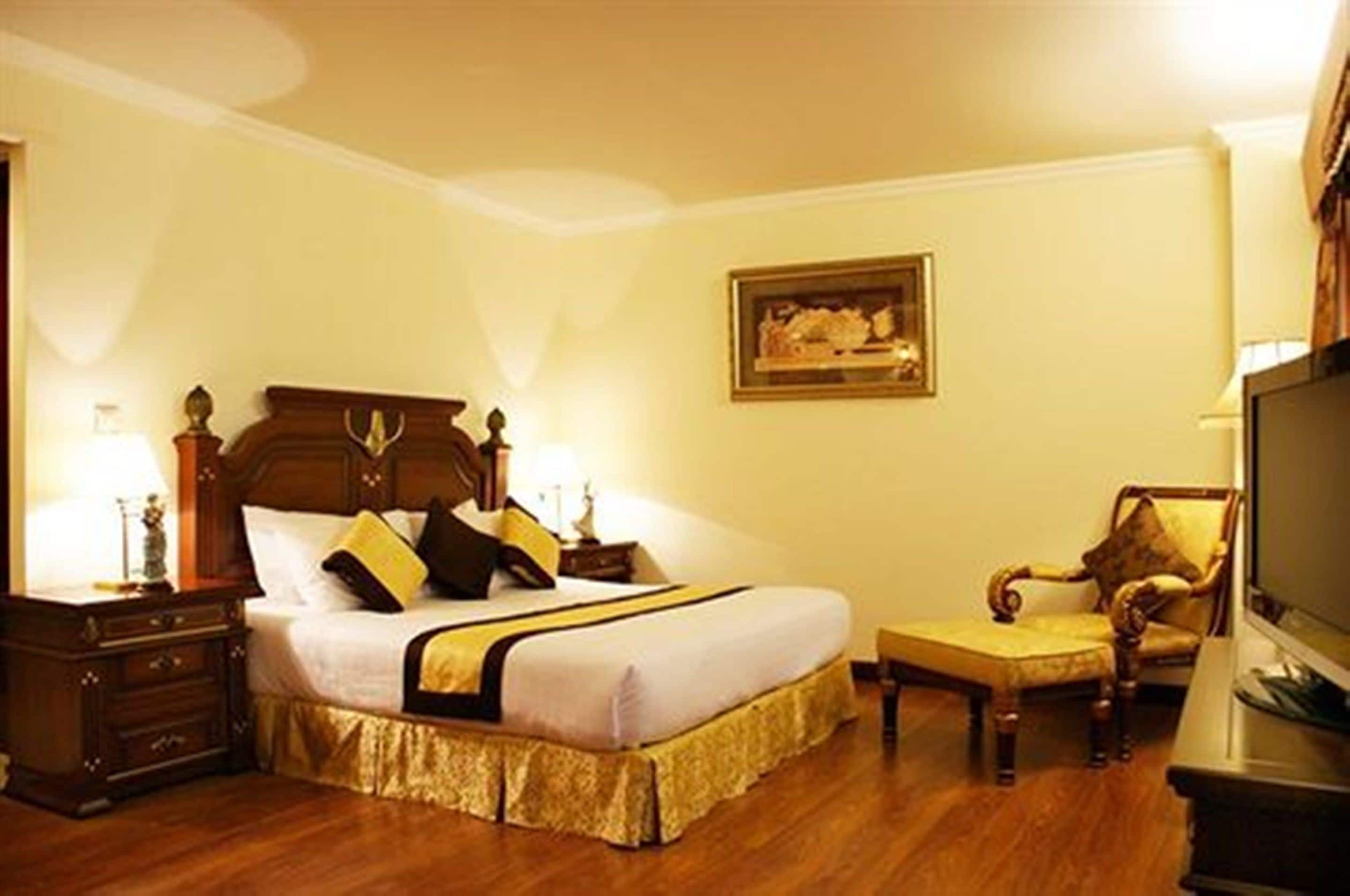 Una habitación de hotel con una cama grande, una mesita de noche de madera, una silla y un televisor.