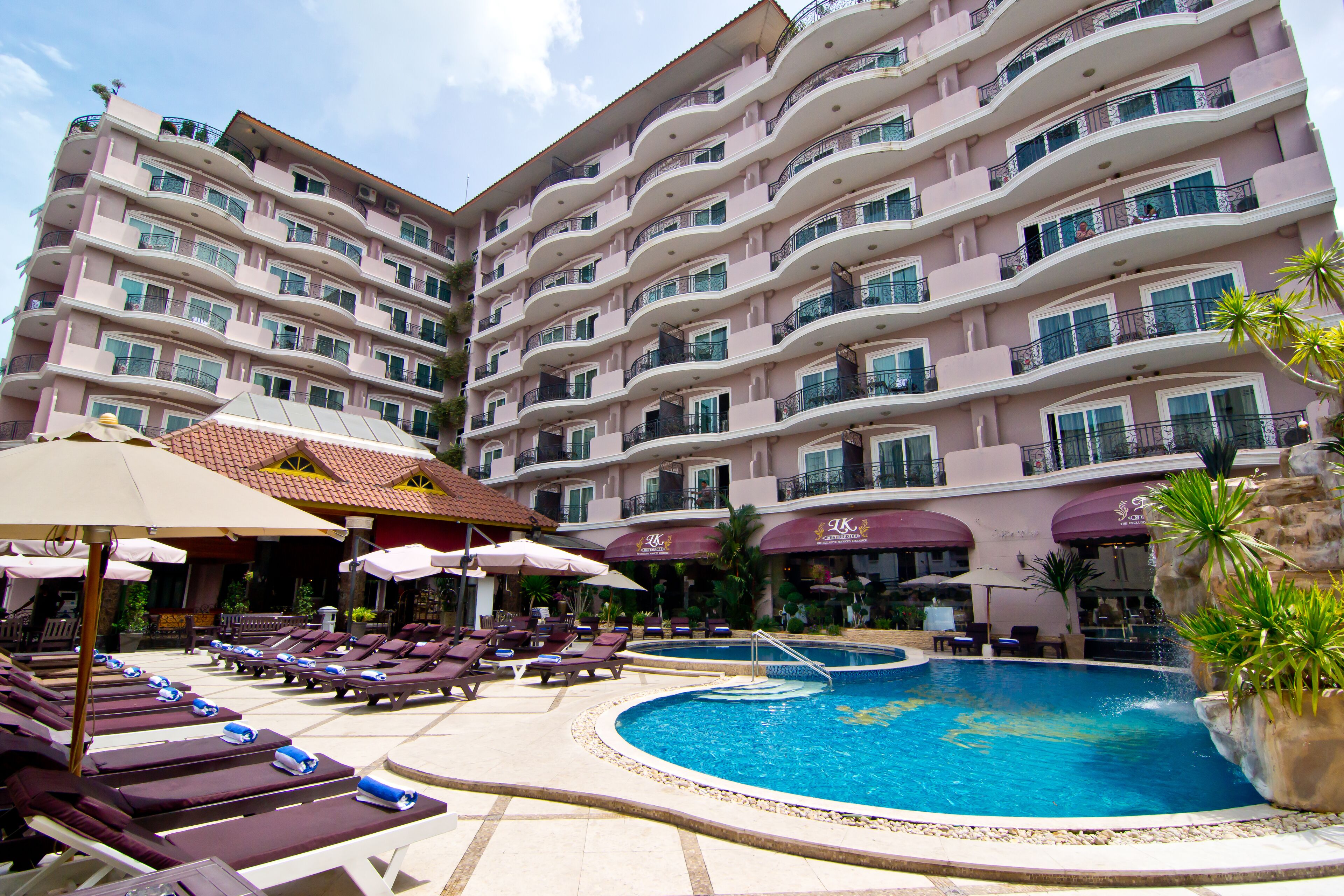 A hotel with multiple balconies, a swimming pool, and sun loungers.